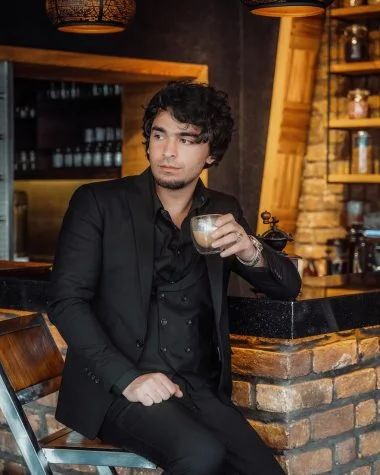 man in black suit jacket holding glass of coffee