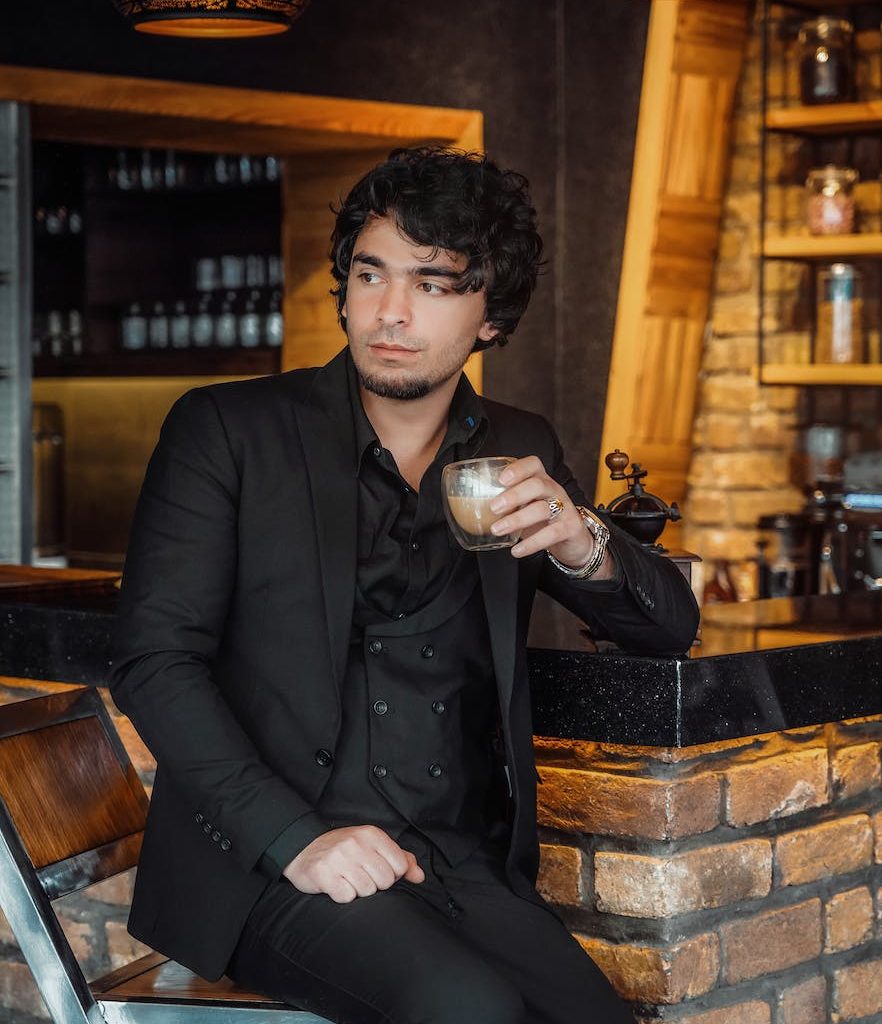 man in black suit jacket holding glass of coffee