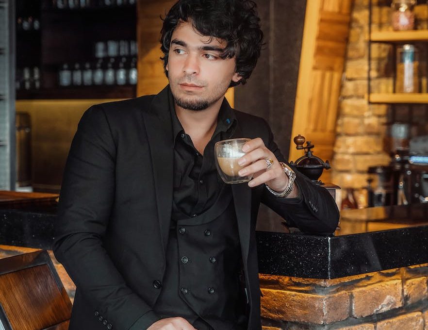 man in black suit jacket holding glass of coffee